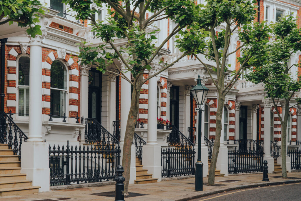 Part brick part stucco fronted row of developed buildings on tree lined street in Prime Central London's Kensington